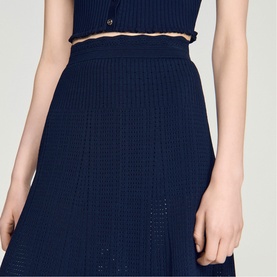 Model wearing Sandro navy blue knit dress with textured pointelle detail and gold-tone chain belt at waist