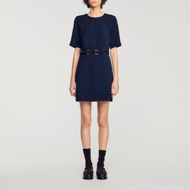 Model wearing Sandro Womens French Dress in navy blue, short sleeves, belted waist with ring detail, mini length, styled with black socks and loafers.