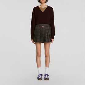 Model wearing Sandro dark grey pleated mini skirt with check pattern, styled with dark knit jumper, white socks and lace-up shoes