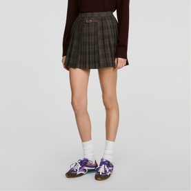 Model wearing Sandro dark grey tartan pleated mini skirt with buckle detail, styled with burgundy knit and purple trainers