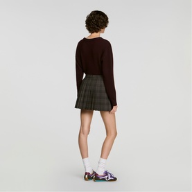 Model wearing Sandro dark grey pleated check mini skirt, styled with dark burgundy knit top and colourful trainers, shot from behind.