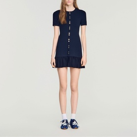 Model wearing Sandro Ruffle Mini Knitted Dress in midnight blue with decorative buttons, round neck, short sleeves, and ruffled hem.