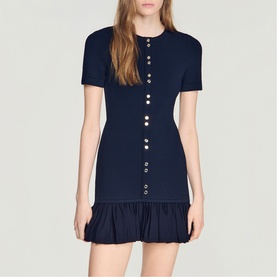 Model wearing Sandro Ruffle Mini Knitted Dress in midnight blue with gold decorative buttons, round neckline, short sleeves and ruffled hem.