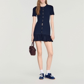 Model wearing Sandro Ruffle Mini Knitted Dress in midnight blue with button front and ruffled hem, styled with burgundy bag and navy trainers.