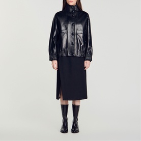Model wearing Sandro black patent faux-leather jacket and midi skirt, styled with knee-high black boots.
