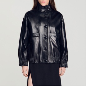 Model wearing Sandro black faux leather bomber jacket with button front, chest pockets, and elasticated cuffs, styled with a black skirt.