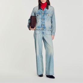 Model carrying Sandro brown clutch bag, styled with light blue denim jacket and wide-leg jeans, red turtleneck