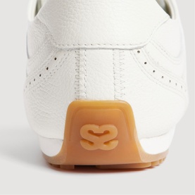 Sandro women's white leather trainer, close-up of heel counter with branded logo detail and tan gum rubber sole.
