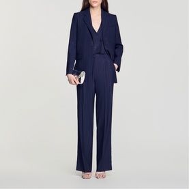 Model wearing navy blue tailored blazer with matching wide-leg trousers and waistcoat, styled with a silver clutch bag