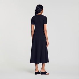 Model wearing Sandro Womens French Dress in black, midi length, short sleeves, flared skirt, shown from behind with black mule sandals.