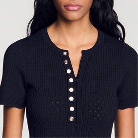 Model wearing Sandro Womens French Dress in black, ribbed knit with short sleeves and gold button placket detail at neckline.