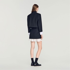 Model wearing Sandro black cropped jacket and mini dress with white frill hem, styled with black loafers and socks, rear view