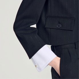 Model wearing Sandro black pinstripe blazer with white French cuffs and matching tailored trousers, hand in pocket.