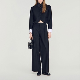 Model wearing Sandro black cropped blazer and wide-leg trousers with white shirt cuffs, styled with small black bag and loafers