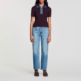 Model wearing burgundy ribbed knit polo top with blue contrast collar, styled with light wash wide-leg jeans and dark brown shoes