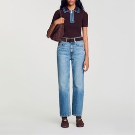 Model wearing dark burgundy knit polo top with blue trim, styled with light wash straight-leg jeans and dark loafers, carrying brown bag