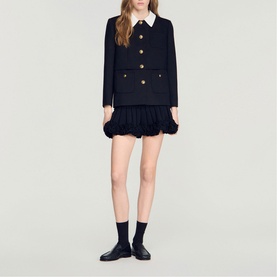 Model wearing Sandro Womens French Dress in black with ruffled hem, gold buttons, white collar detail, styled with black ankle socks and loafers.