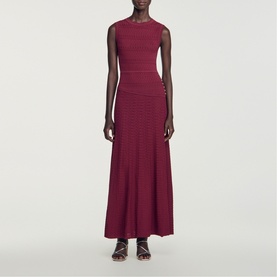 Model wearing Sandro Womens French Dress in red, sleeveless maxi knit style with ribbed texture and side button detail, styled with strappy sandals