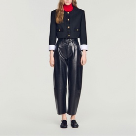 Model wearing Sandro black cropped military-style jacket with gold buttons and white cuffs, styled with black leather trousers and loafers