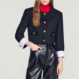 Model wearing Sandro black cropped jacket with gold buttons and white cuff detail, styled with red turtleneck and black leather trousers