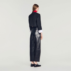 Model wearing Sandro black leather wide-leg trousers, styled with a cropped dark jacket, red collar top and black loafers, rear view.