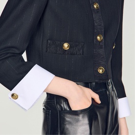 Model wearing Sandro black jacket with gold buttons and white cuffs, styled with black leather trousers