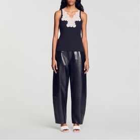 Model wearing Sandro Lace Trim Ribbed Tank Top in black with white lace trim neckline, styled with black wide-leg leather trousers and white slides.