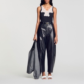 Model wearing Sandro Lace Trim Ribbed Tank Top in black with white lace trim, styled with black faux-leather trousers and white sandals.