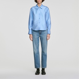 Model wearing Sandro sky blue long-sleeve shirt with pointed collar, styled with light wash straight-leg jeans and black shoes.