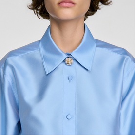 Model wearing Sandro sky blue satin shirt with pointed collar and embellished floral button detail at neckline
