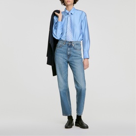 Model wearing Sandro sky blue oversized shirt with striped tie detail, styled with light wash straight-leg jeans and black loafers.