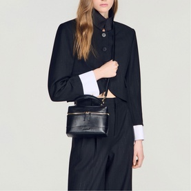 Model carrying Sandro black structured mini bag with gold-tone hardware, styled with black cropped blazer and wide-leg trousers