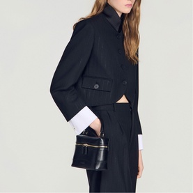 Model carrying Sandro black small structured top-handle bag with gold zip detail, styled with cropped dark blazer and wide-leg trousers.