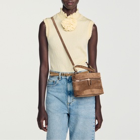 Model carrying Sandro brown suede crossbody bag with gold-tone hardware and adjustable strap, styled with cream top and blue jeans