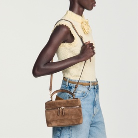 Model carrying Sandro brown suede crossbody bag with gold-tone hardware, styled with cream knit top and blue jeans