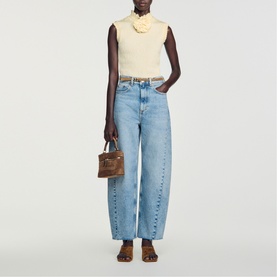 Model carrying Sandro brown small top-handle bag with gold-tone hardware, styled with light-wash wide-leg jeans and cream sleeveless top