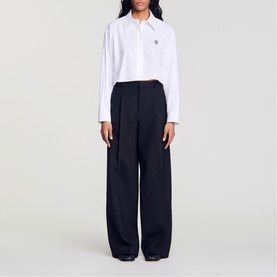 Model wearing Sandro Pinstripe High-Rise Wide Leg Trousers in black with wide-leg silhouette and pleat details, styled with a white shirt.