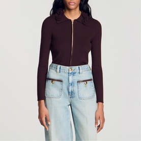 Model wearing Sandro brown ribbed zip-up cardigan with ruffle collar, styled with light wash wide-leg jeans.