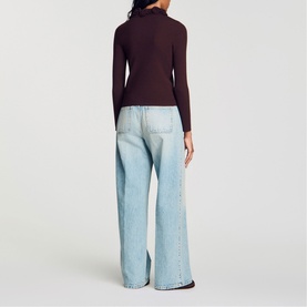 Model wearing Sandro brown ribbed roll-neck top, back view, styled with light wash wide-leg jeans.
