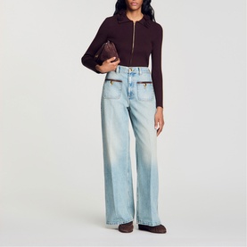 Model wearing Sandro brown zip-up ribbed cardigan, styled with light blue wide-leg jeans and carrying a dark brown clutch bag.