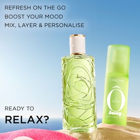 Lanc&ocirc;me &Ocirc; Oui Juicy body mist in green spray bottle alongside matching green glass fragrance bottle, on sandy beach background