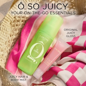 Lanc&ocirc;me &Ocirc; So Juicy Hair & Body Mist in green bottle alongside Juicy Gloss lip product, styled on pink gingham fabric with straw hat