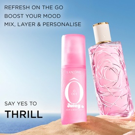 Lanc&ocirc;me &Ocirc; Oui Juicy body mist in pink pump bottle styled with matching pink rose-embossed fragrance bottle against a blue sky backdrop