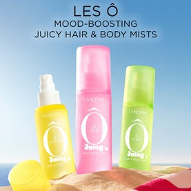 Lanc&ocirc;me Les &Ocirc; Juicy Hair & Body Mists in yellow, pink and green bottles arranged on sand with blue sky background.