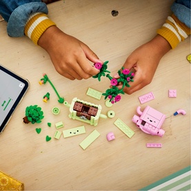 Lego Botanical set being assembled by child's hands, with pink pig, green tree, and floral pieces spread on a wooden table