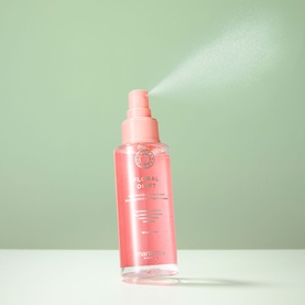 Maria Nila hair mist spray bottle in pink with pump nozzle, shown dispensing a fine mist against a sage green background