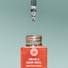 Maria Nila Head & Hair Heal Soothing Serum in orange glass bottle with dropper dispensing a drop of serum