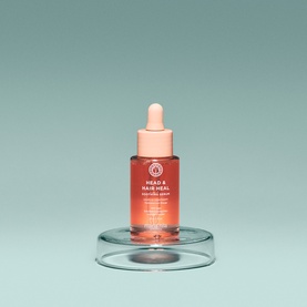 Maria Nila Head & Hair Heal Scalp Serum in a coral-pink dropper bottle displayed on a glass disc stand