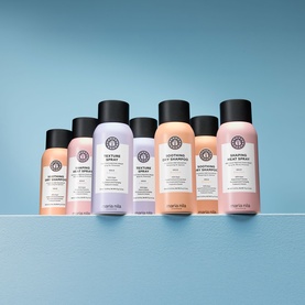 Maria Nila hairspray collection in travel and full sizes, featuring pink, lilac and peach spray bottles with black caps on blue background