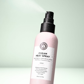 Maria Nila Cream Heat Spray in pink bottle with pump dispenser, shown with mist of product being sprayed against mint green background
